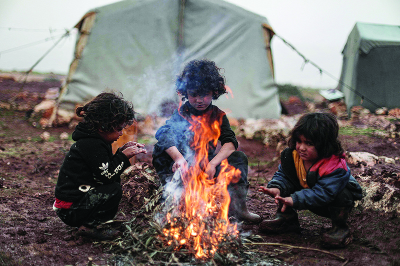 BABISQA, Syria: Children warm up around a bonfire at a makeshift camp for the displaced in Syria’s northwestern province of Idlib on Dec 17, 2021. — AFP