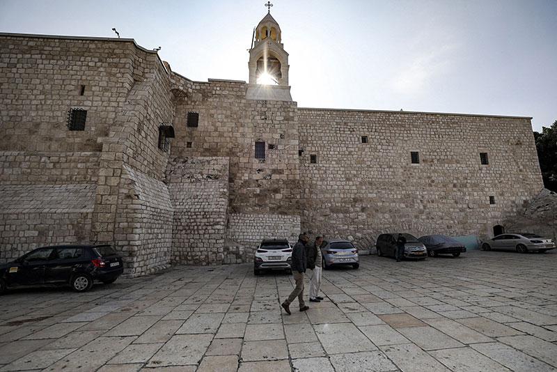 BETHLEHEM: Two men walk in the empty Manger Square outside the Church of the Nativity, as the square remains devoid of pilgrims less than two weeks before Christmas. - AFP