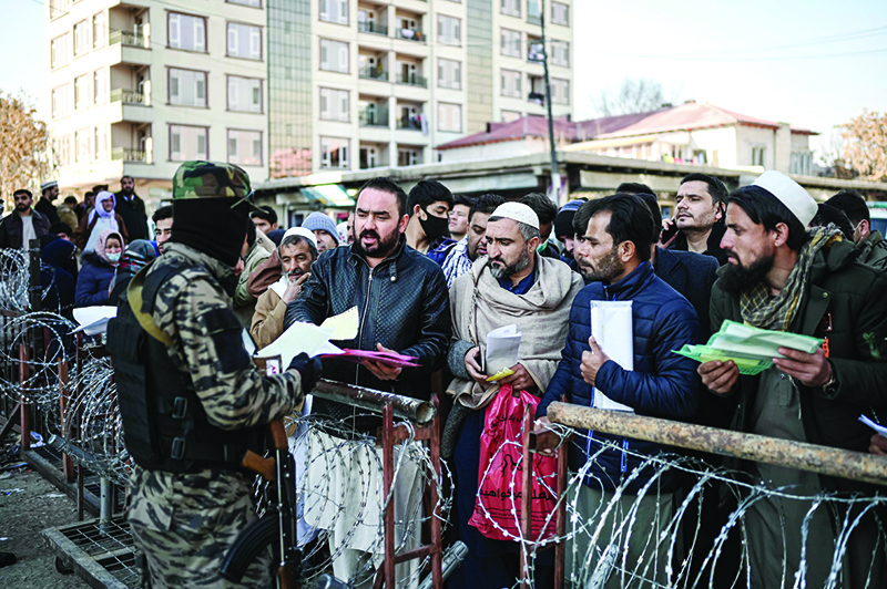 KABUL: A Taleban fighter (R) inspects documents of people queuing to enter the passport office in Kabul yesterday. — AFP