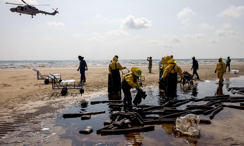 RAYONG, Thailand: A helicopter flies overhead as workers clean up crude oil on Mae Ram Phueng beach following a spill caused by a leak in an undersea pipeline owned by Star Petroleum Refining Public Company Limited (SPRC) in Rayong on Sunday. — AFP