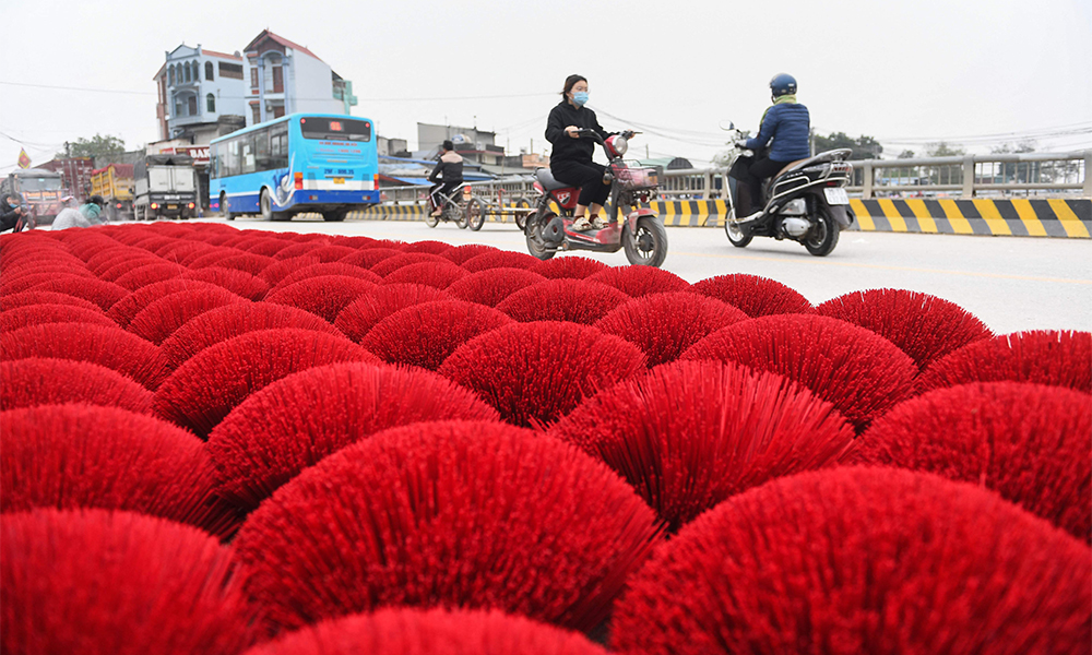 Residents ride past incense sticks drying on a street in Quang Phu Cau village on the outskirts of Hanoi.