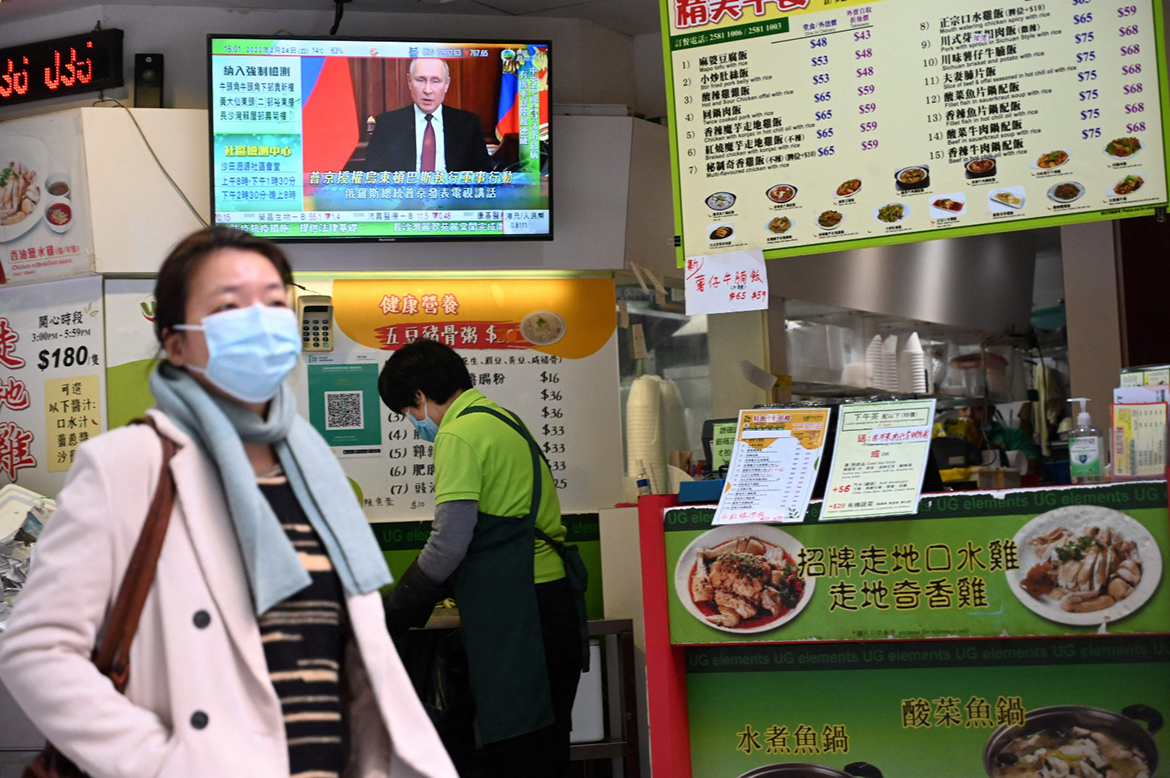 A woman chops vegetables as another passes by as Russian President Vladimir Putin is seen on TV news in a restaurant in Hong Kong on February 24, 2022 as his troops invade Ukrainian territory. - AFP