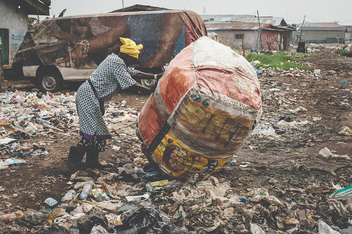 LAGOS: In this file photo, a woman pushes a sack containing recycled plastic bottles past an area where plastic waste is being used to reclaim a swamp so that the land can be developed for housing in the Mosafejo area of Lagos. -- AFP
