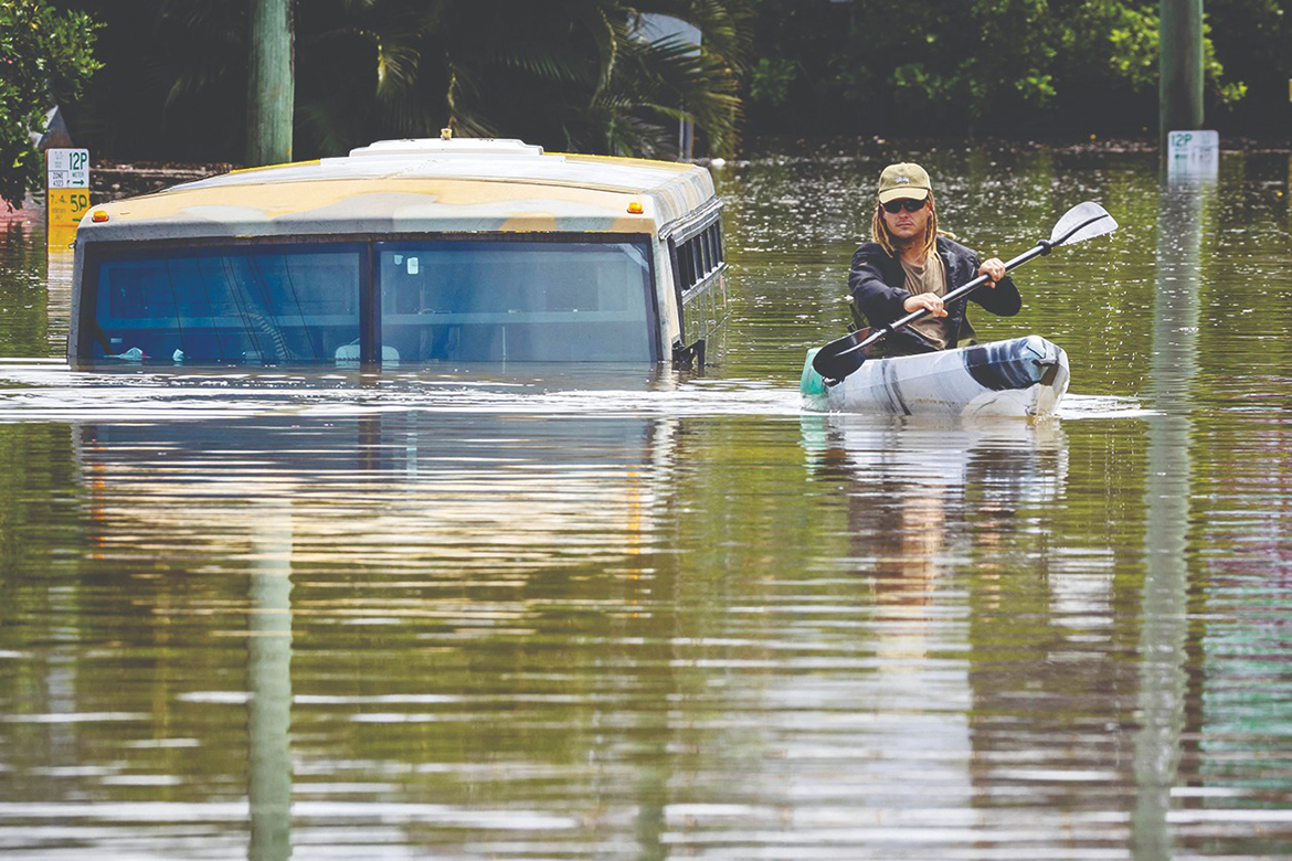 BRISBANE: A man paddles his kayak next to a submerged bus on a flooded street in the town of Milton in suburban Brisbane yesterday. - AFP