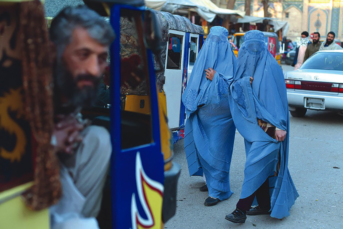 HEART:  A rickshaw taxi driver looks on as burqa clad-women walk a long road, in Heart. – AFP