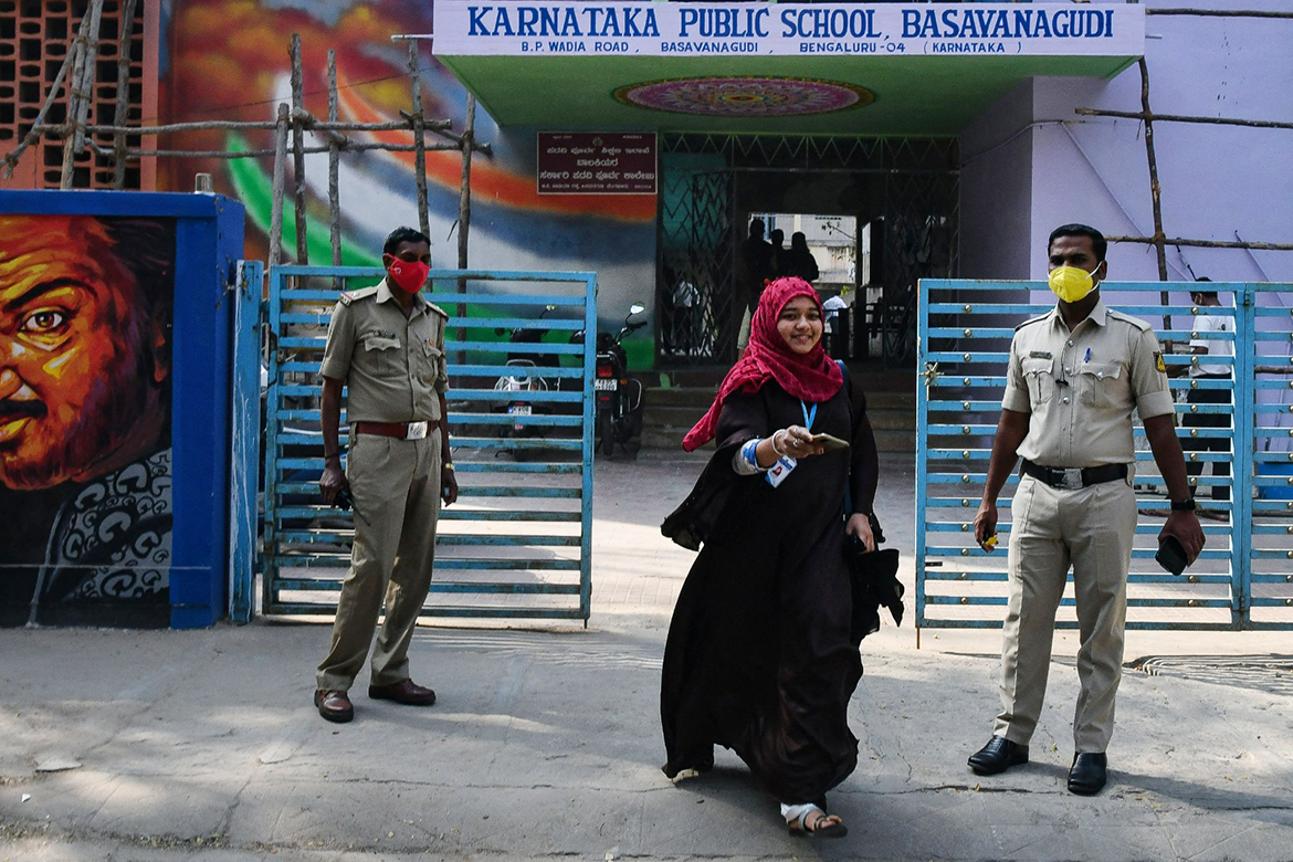 BANGALORE: Police stand guard as a student of a government high school and pre-university college for women steps out to return a phone to her parents standing outside yesterday. – AFP