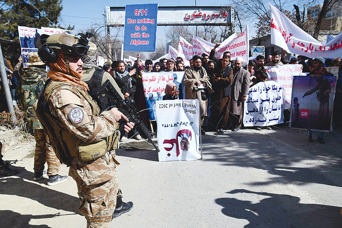 KABUL: A member of the Taleban Badri 313 military unit (L) stands guard as people hold placards during a protest against the recent remarks by US President Joe Biden to freeze Afghanistan's assets, in Kabul yesterday. - AFP