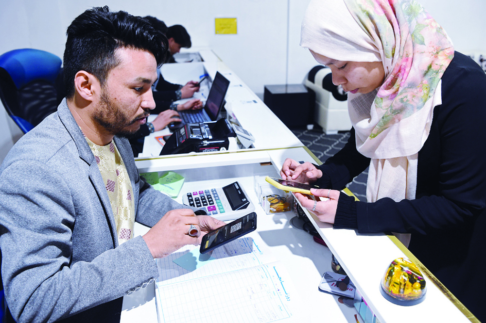 HERAT: In this photo taken on February 15, 2022, university student Arezo Akrimi (right) exchanges cryptocurrency for cash at a currency exchange office in Herat. Since the Taleban returned in August 2021, Afghanistan's economy has virtually collapsed and the country is in the grip of a crisis caused by the seizure of billions of dollars of assets held abroad.-AFP nn