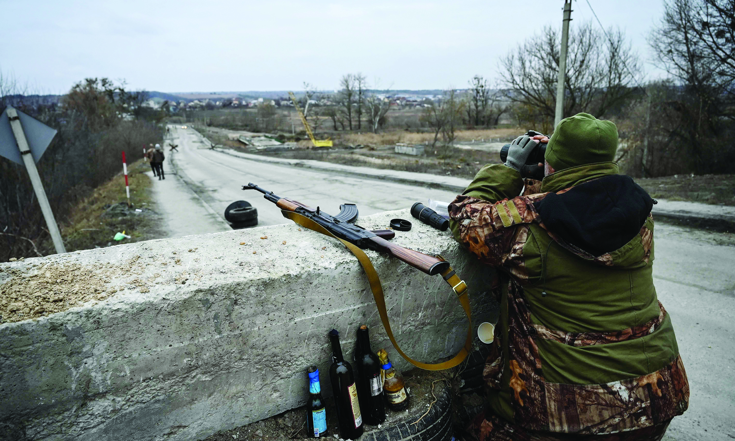 STOYANKA, Ukraine: A Ukrainian serviceman looks through binoculars towards the town of Stoyanka yesterday at a checkpoint before the last bridge on the road that connects Stoyanka with Kyiv. - AFP n