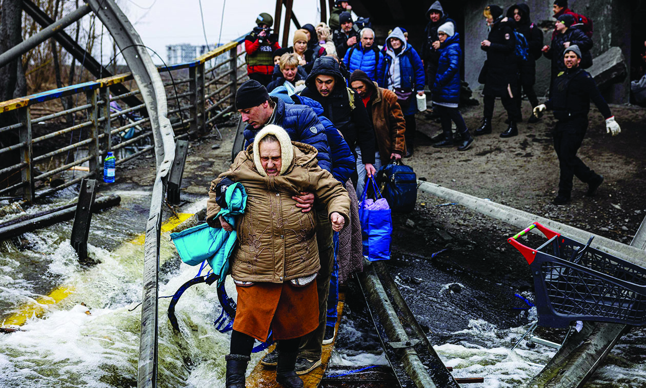 IRPIN, Ukraine: A man helps a woman evacuee cross a destroyed bridge as she and others flee this city northwest of Kyiv yesterday. – AFP n