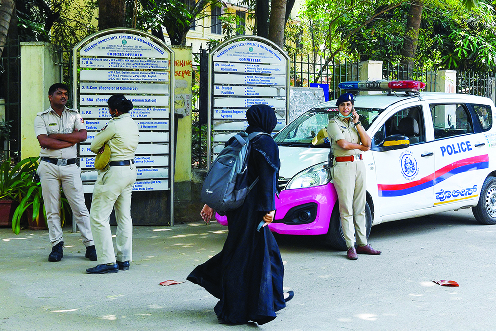 BANGALORE: A girl wearing a hijab walks past police guarding outside a school yesterday after a court upheld a local ban on the hijab in classrooms. - AFP n