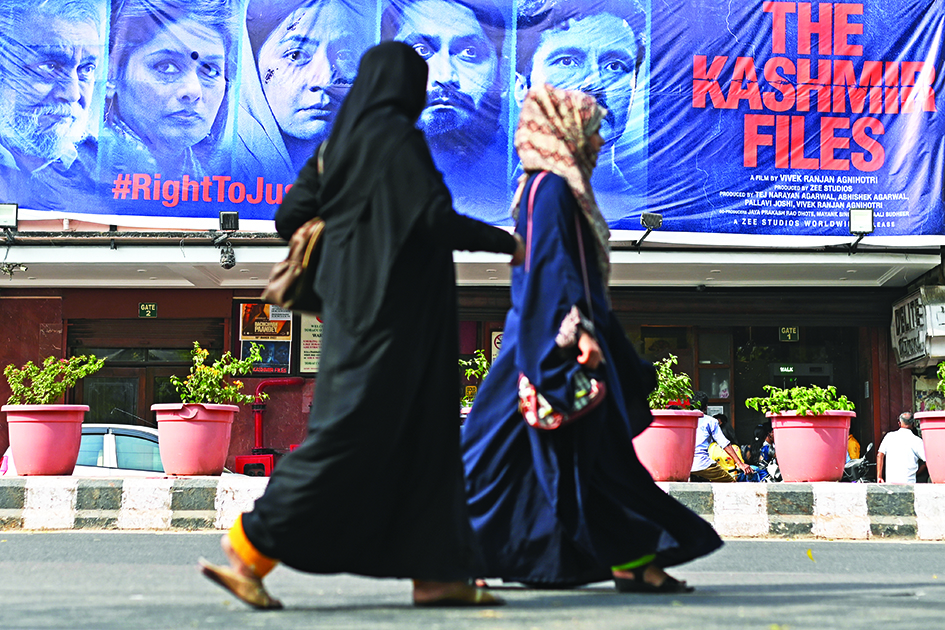 In this file photo women walk past a banner of Bollywood movie 'The Kashmir Files' installed outside a cinema hall in the old quarters of Delhi.—AFP photos