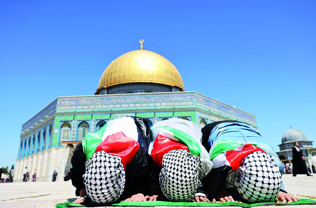 JERUSALEM: Palestinian girls, wearing national flags and checkered 'kafiyeh' headdresses kneel to pray in front of the Dome of Rock mosque at the Al-Aqsa mosque compound in Jerusalem's Old City. - AFP