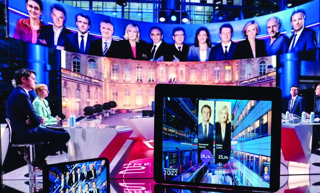 TOULOUSE: Photograph taken in Toulouse, on April 10, 2022 shows screens displaying TV shows showing the projected results after the close of polling stations in the first round of the French presidential election. - AFP