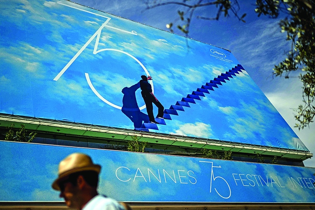 A man wearing a hat passes by the official poster of the 75th Cannes Film Festival at the Palais des Festivals main entrance in Cannes, southeastern France.—AFP photos