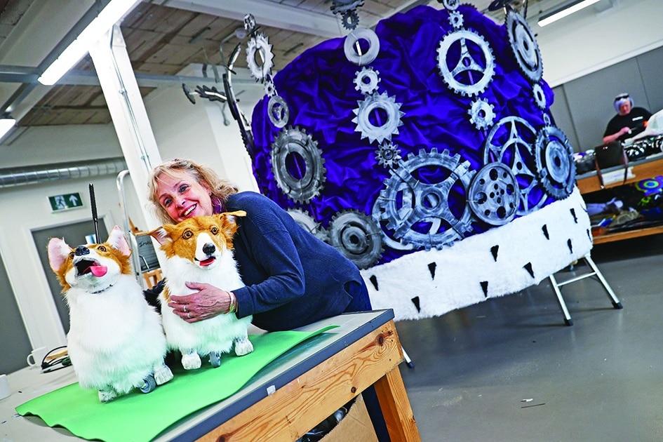 Jane Hytch, Chief Executive of Imagineer, hugs a life-sized model of a corgi dog beside a giant model of a crown in the company's workshop.