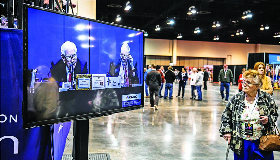 OMAHA: A woman looks at the screen with a live view of Berkshire Hathaway CEO Warren Buffett (left) and Vice Chairman Charlie Munger  at the Berkshire Hathaway Shareholders Meeting at CHI Health Center in Omaha, Nebraska on April 30, 2022. – AFP