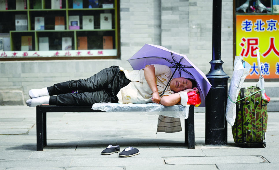 BEIJING: A man rests on a bench while sheltering under an umbrella, along a road in Beijing on June 30, 2022. - AFP
