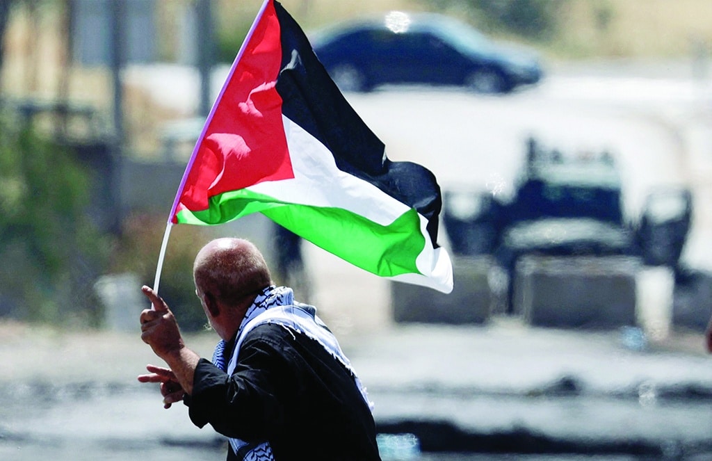 BEITA: A Palestinian protester waving a national flag flashes the victory sign as he faces Zionist security forces during clashes with them in the West Bank town of Beita, south of Nablus.- AFP