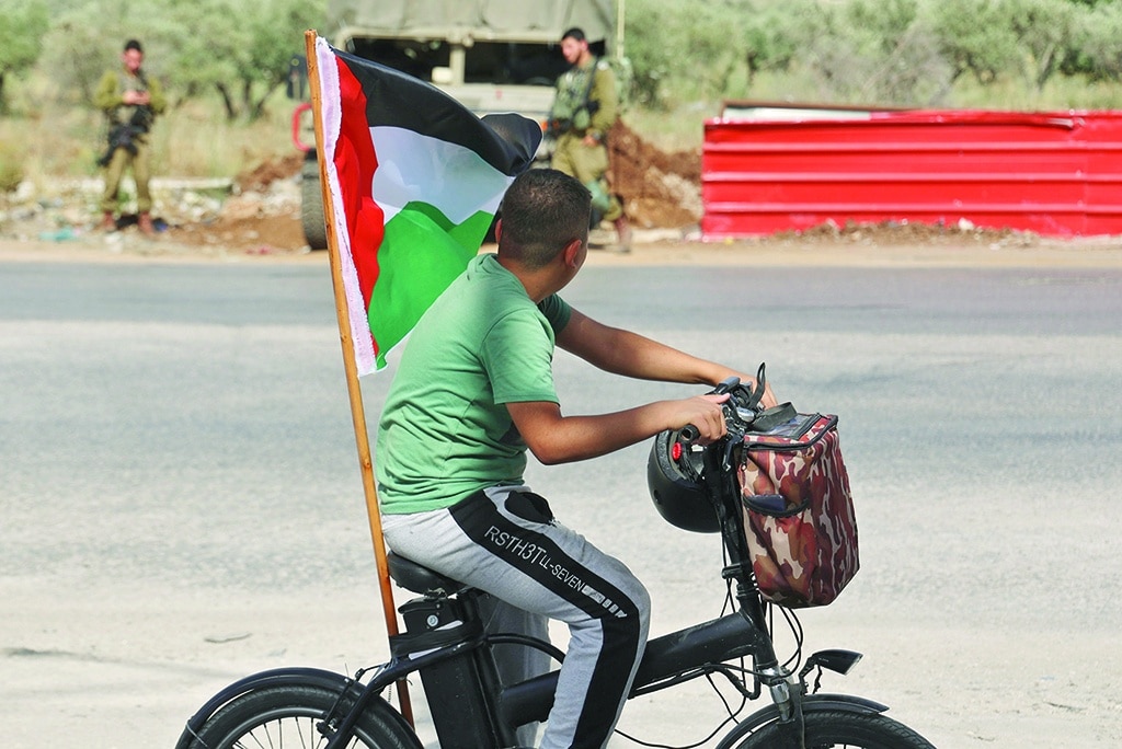HUWARA, Palestinian Territories: A young boy rides a bicycle showing a Palestinian flag in the town of Huwara near Nablus in the occupied West Bank. - AFP