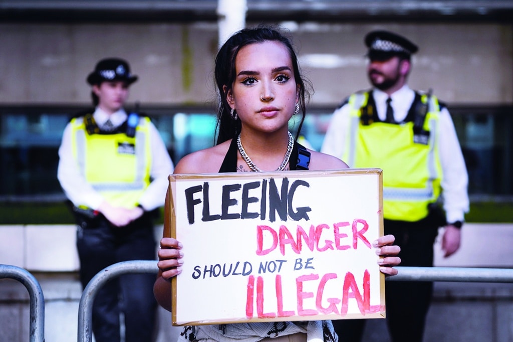 LONDON, United Kingdom: A protester holds a placard as she stands outside the Home Office in central London on June 13, 2022, to demonstrate against the UK government's intention to deport asylum-seekers to Rwanda. - AFP
