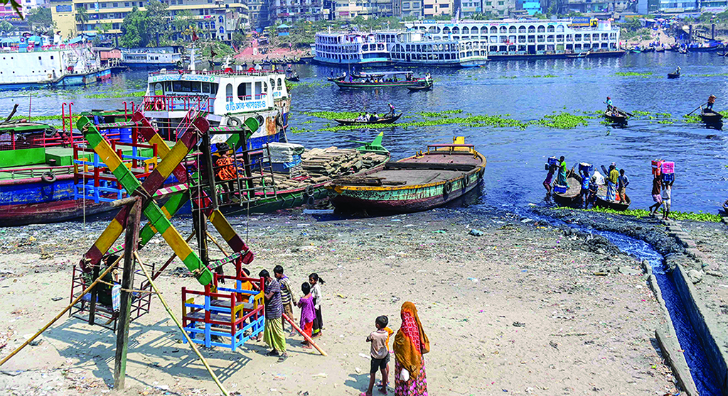 DHAKA: In this picture, industrial effluents enter the waters of the Buriganga River as children wait to board a Ferris wheel ride along the river bank in Karanigonj, on the outskirts of Dhaka. - AFP