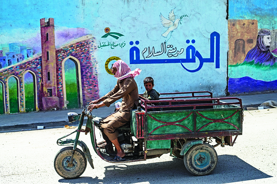 RAQA: A man and his son commute in a motorized cargo tricycle in Syria's northern city of Raqa.- AFP