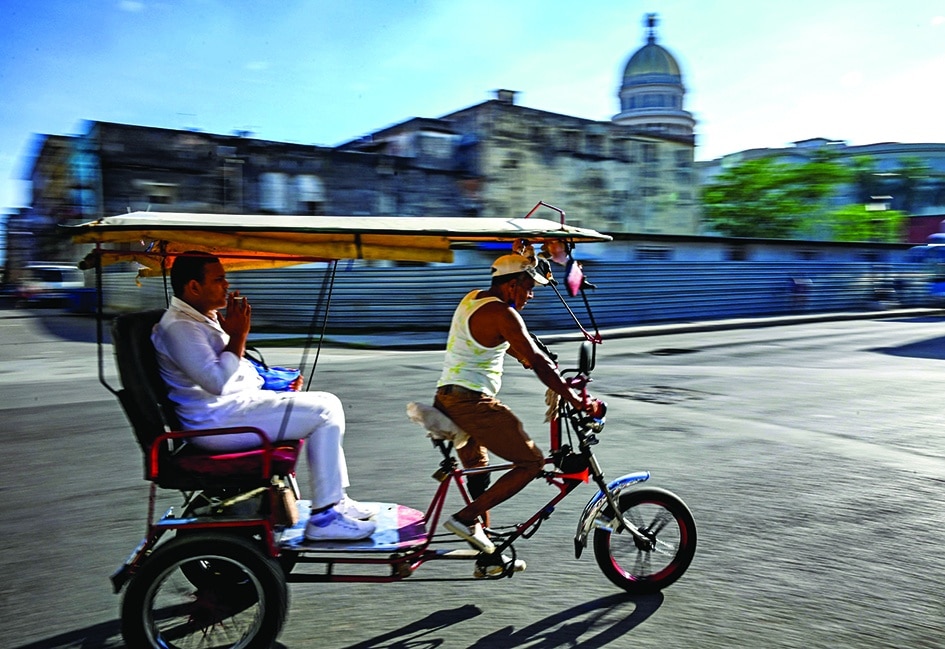 HAVANA: Men ride on a bicitaxi along a street of Havana.- AFP