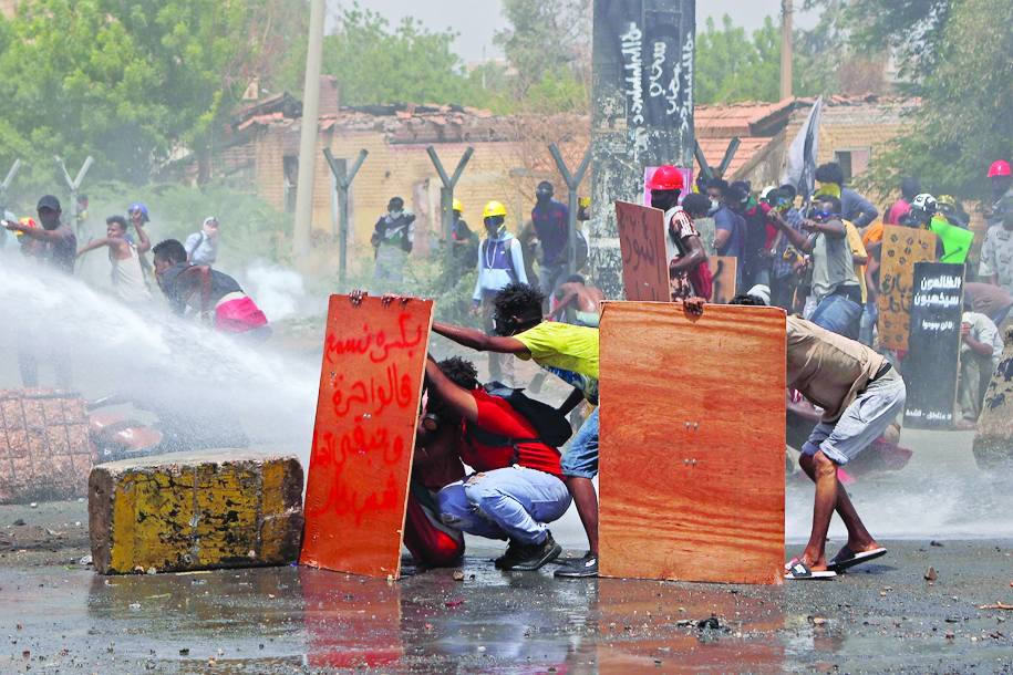 KHARTOUM, Sudan: Anti-coup protesters take cover as riot police try to disperse them with water cannon during a demonstration against military rule in the centre of Sudan's capital Khartoum. - AFP