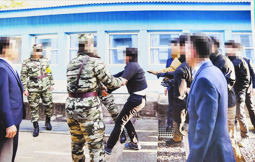 This undated handout photo provided by the South Korean Unification Ministry on July 13, 2022, shows shows (C, wearing black), one of two alleged North Korean mass murderers who were controversially deported by Seoul in 2019, appearing to physically resist as authorities try to hand him over to Pyongyang officials, via the truce village of Panmunjom. - AFP
