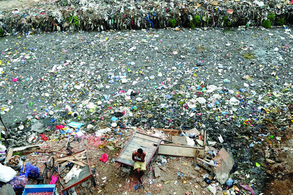 NEW DELHI: A man sits on a cart next to a sewer canal filled with plastics and other waste on June 30, 2022. - AFP
