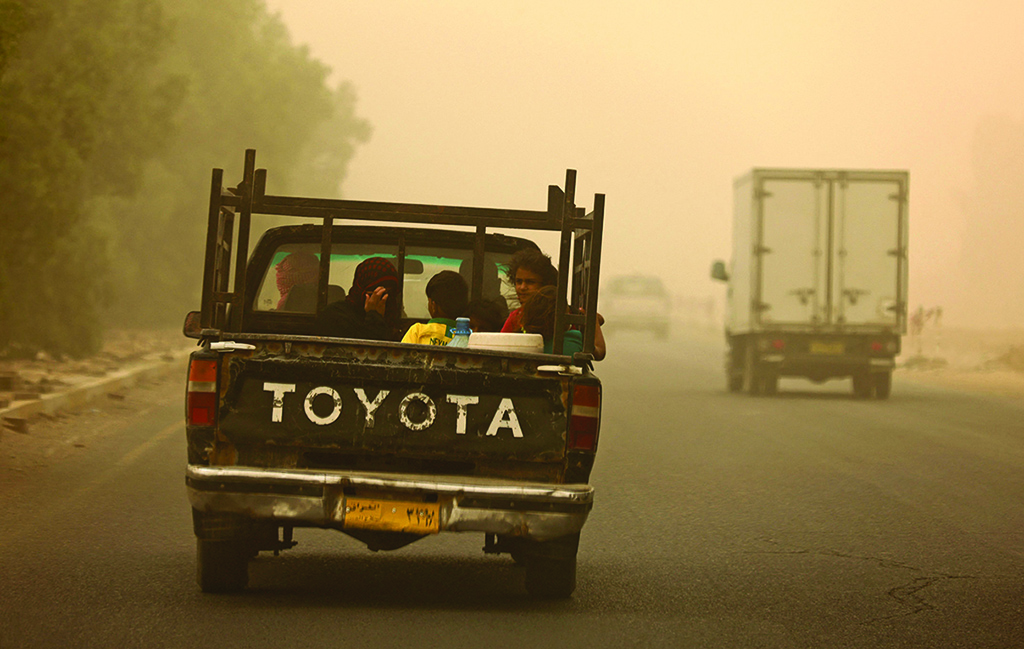 KHALES, Iraq: A family rides in the back of a pickup truck during a sandstorm in this town in Diyala province on July 3, 2022. - AFP