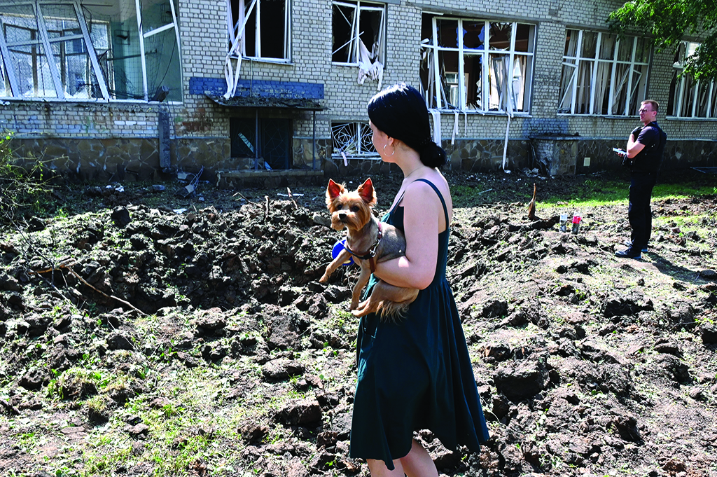 KHARKIV, Ukraine: A woman holding a dog stands by a huge crater made from the hit of a rocket close to the destroyed school building in Kharkiv. - AFP