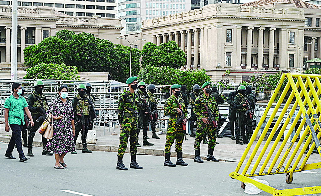 COLOMBO: People walk past army personnel standing guard in front of the Presidential Secretariat in Colombo on July 23, 2022. - AFP
