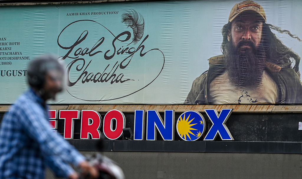 A man rides his bike as he walks past a poster of the upcoming new Bollywood film 'Laal Singh Chaddha' put up at the Metro theatre in Mumbai.— AFP photos