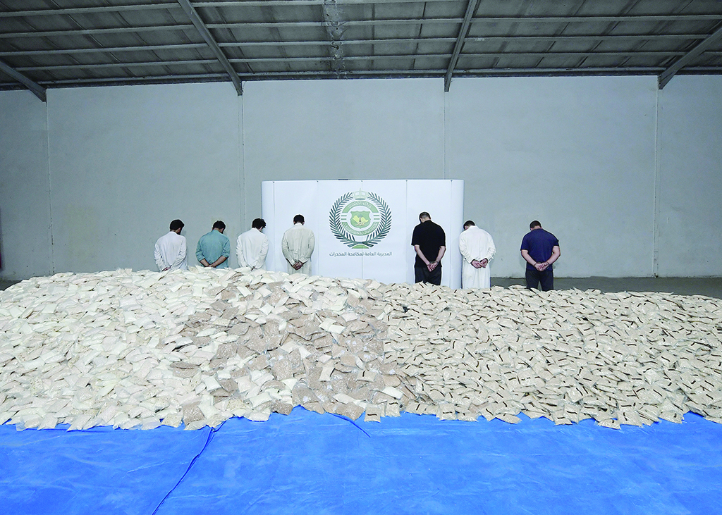 A handout picture released by the Saudi interior ministry on August 31, 2022 shows handcuffed suspects and bags of amphetamine pills on display at a warehouse in a undisclosed location. – AFP