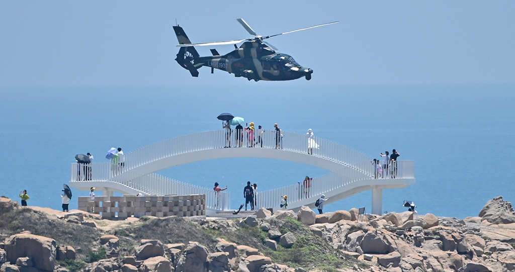PINGTAN, China: Tourists look on as a Chinese military helicopter flies past Pingtan island, one of mainland China's closest point from Taiwan, in Fujian province, ahead of massive military drills off Taiwan. – AFP