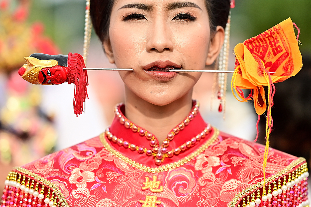 A devotee of the Jor Soo Gong Naka shrine with a skewer pierced through her cheek takes part in a procession during the annual Vegetarian Festival in Phuket. — AFP photos