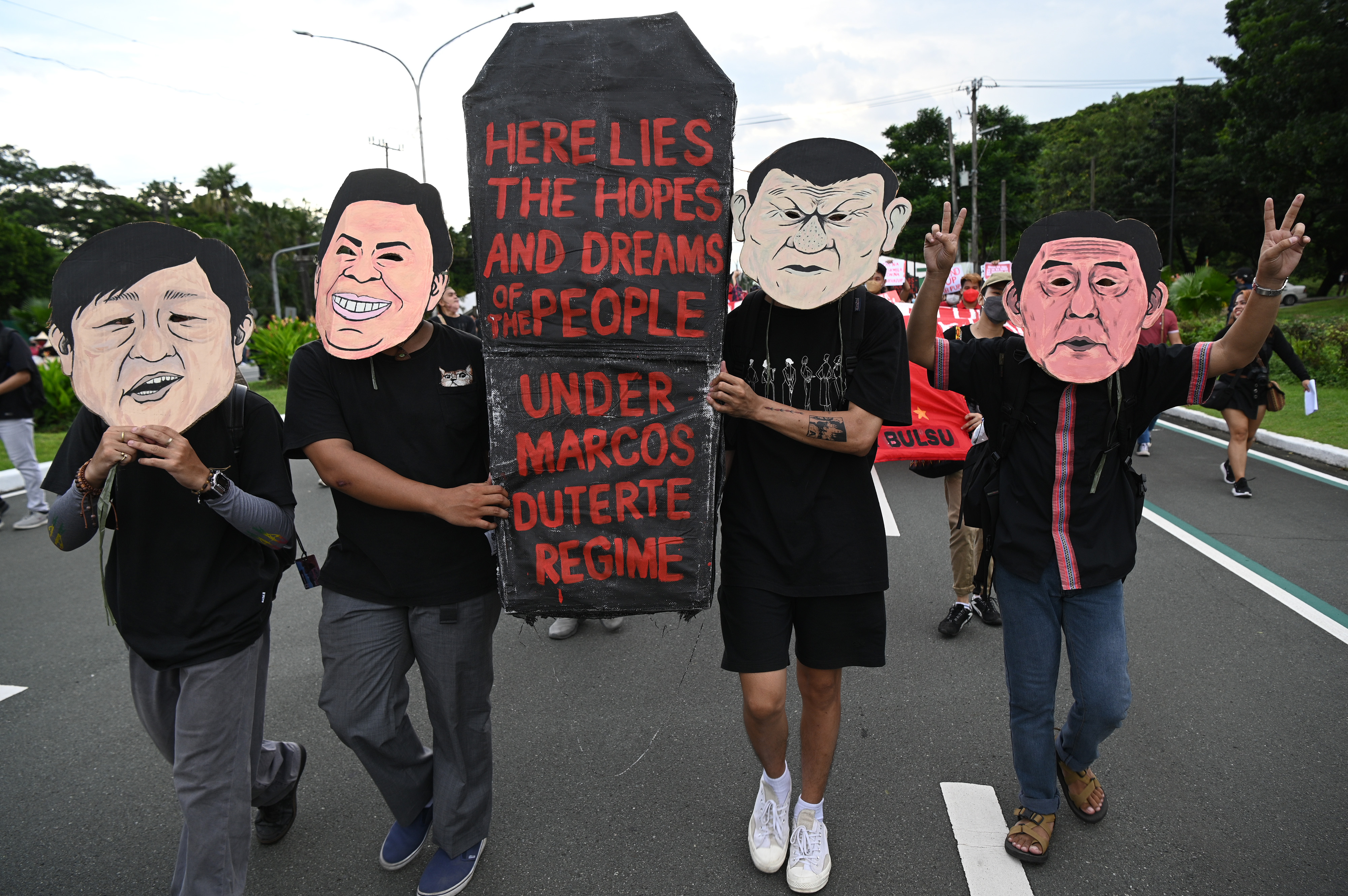 Protesters wearing masks depicting President Ferdinand Maros Jr., and former president Rodrigo Duterte, carry a placard during a rally to commemorate 50 years anniversary of the imposition of martial law at the university grounds in Quezon City, suburban Manila on September 21, 2022. - Philippine human rights activists called on President Ferdinand Marcos Jr to recognise the abuses carried out during his dictator father's brutal rule, as they commemorated on September 21 the 50th anniversary of the start of martial law. (Photo by Ted ALJIBE / AFP)