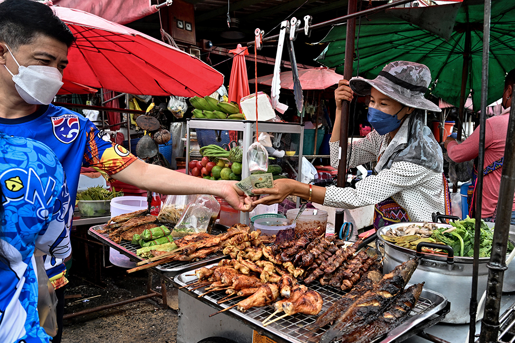 BANGKOK: This photo taken on September 20, 2022 shows a customer paying a vendor at a food cart in a fresh market in Bangkok. - AFP