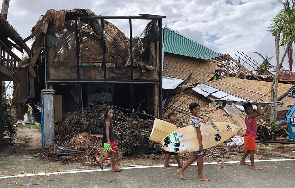 GENERAL LUNA, Philippines: In this photo taken on December 29, 2021, young residents carrying their surf boards, walk past houses destroyed by super Typhoon Rai, as they head for the beach in General Luna town, Siargao island, more than a week after the super typhoon devastated the island. - AFP
