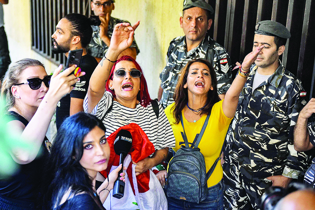 BEIRUT: A reporter looks on as people chant slogans next to security forces standing guard outside a bank held up by a depositor in the Ramlet al-Bayda area of the capital on Sept 16, 2022. - AFP