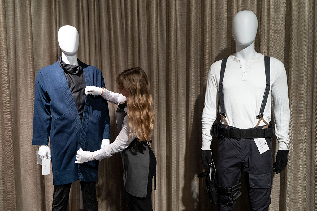 A Christie's employee adjusts a costume (left) worn by actor Rami Malek next to another worn by Daniel Craig in the film 
