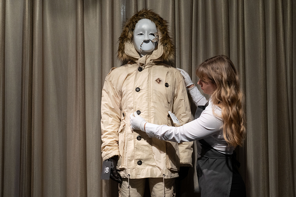 A Christie's employee adjusts a costume and cracked mask worn by actor Rami Malek in the film 