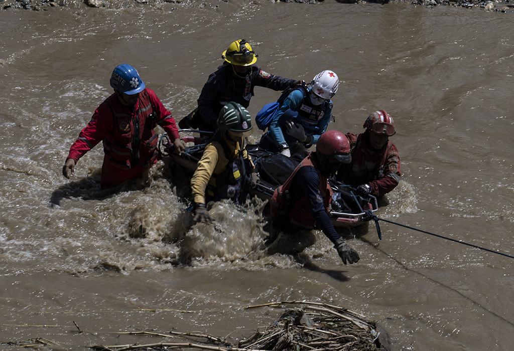 LAS TEJERIAS, Venezuela: Rescuers from different firefighting and Red Cross institutions cross the Tuy river carrying one of two corpses recovered amid debris swept by the river days after a devastating landslide in the Venezuelan town of Las Tejerias. - AFP