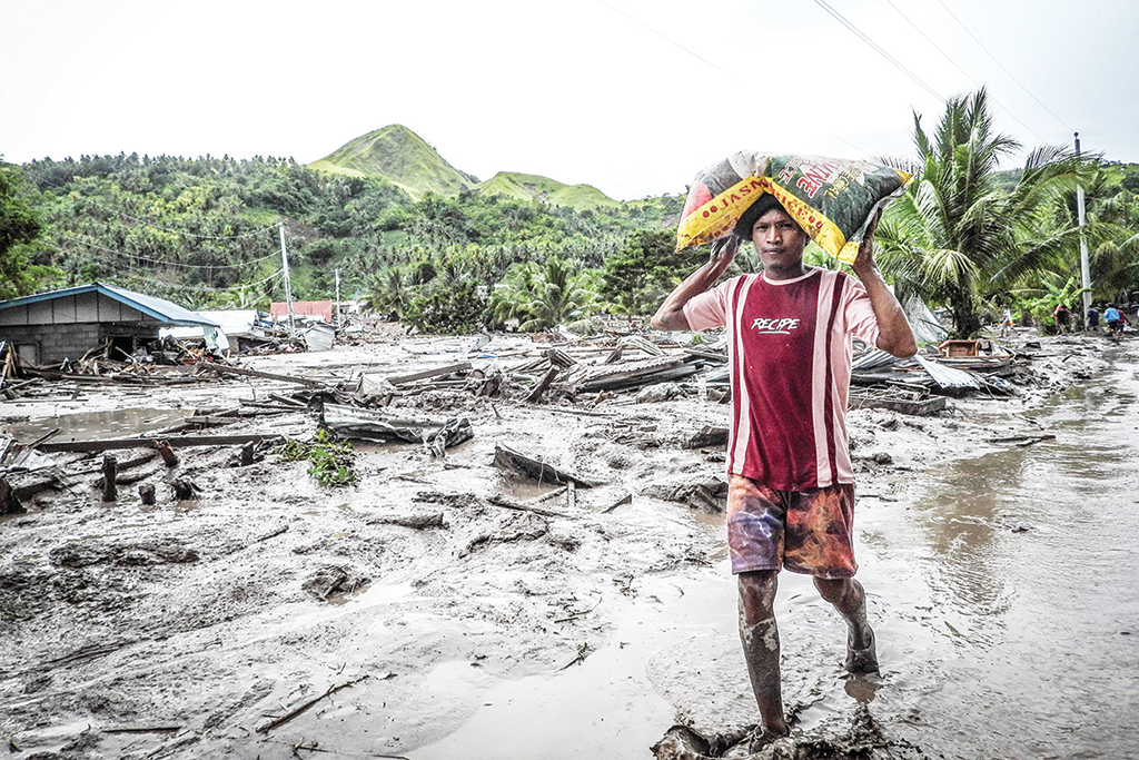 DATU ODIN SINSUAT, Philippines: A resident carrying a sack of rice walks along a muddied road next to a destroyed house in the landslide-hit village of Kusiong in Maguindanao province on Oct 29, 2022. - AFP