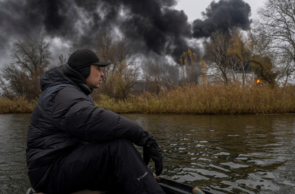 KHERSON: A fisherman sails his boat on the Dnipro River as black smoke rises after an attack on an oil reserve in Kherson amid the Russian invasion of Ukraine. - AFP