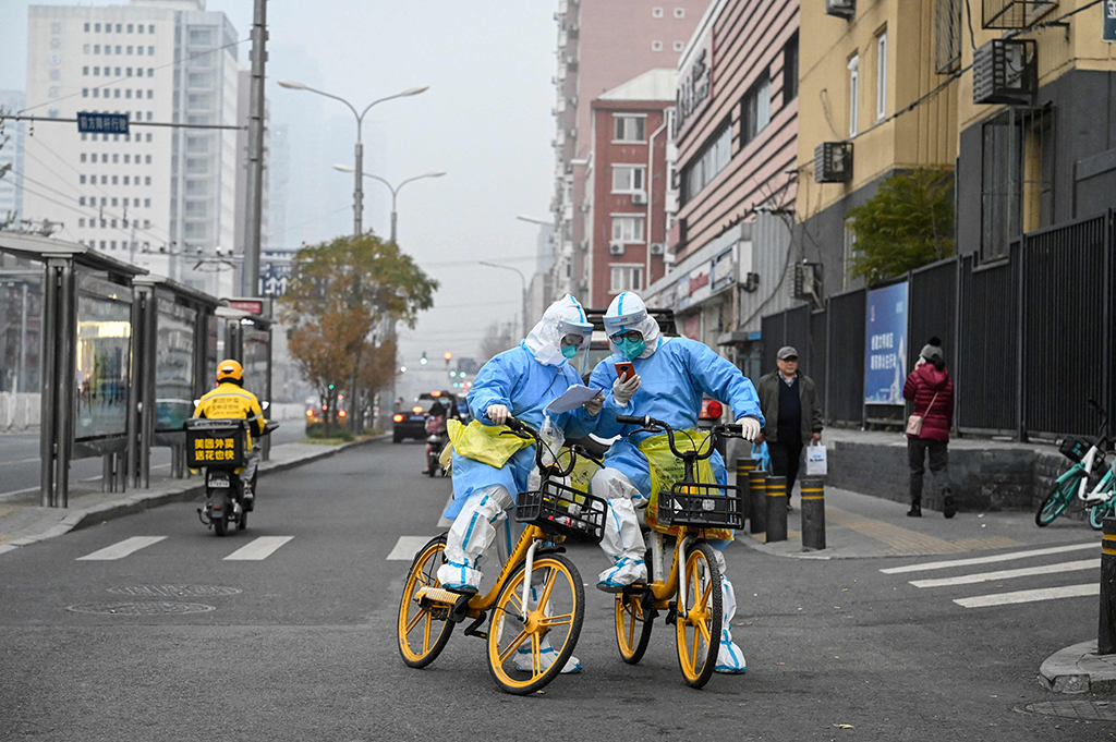 BEIJING: Health workers in personal protective equipments (PPE) carrying COVID-19 coronavirus testing swabs and tubes are seen on bicycles along a street in Beijing on November 24, 2022. - AFP