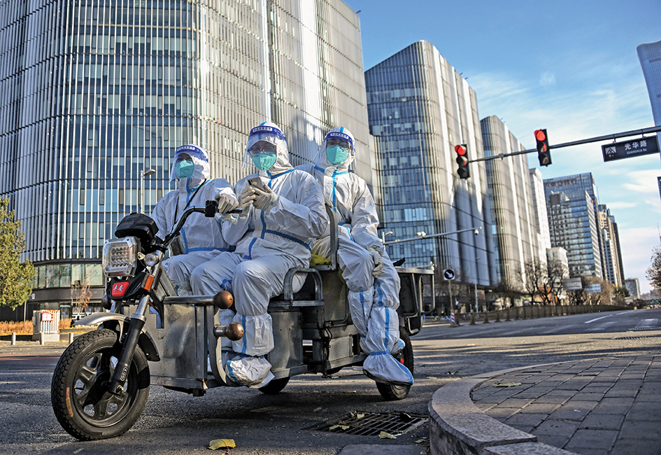 BEIJING: Workers wearing personal protective equipment (PPE) ride on a tricycle along a street in Beijing on November 26, 2022. - AFP