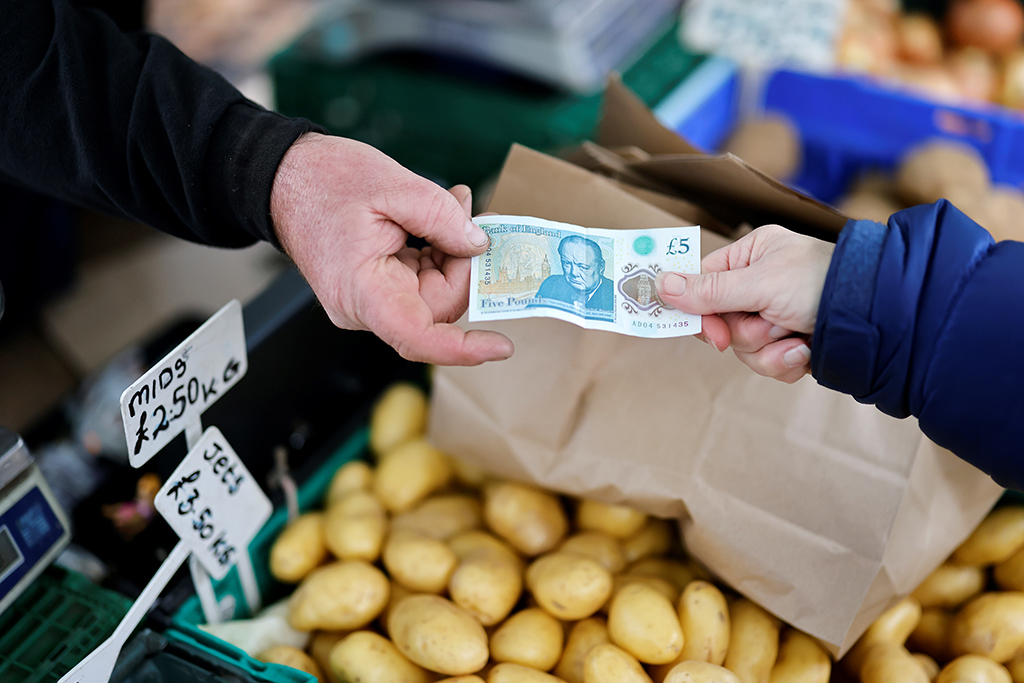 LONDON: In this file photo taken on November 21, 2021, a customer (right) pays a stallholder a five pound note for fruit and vegetables at Walthamstow Market in east London.— AFP
